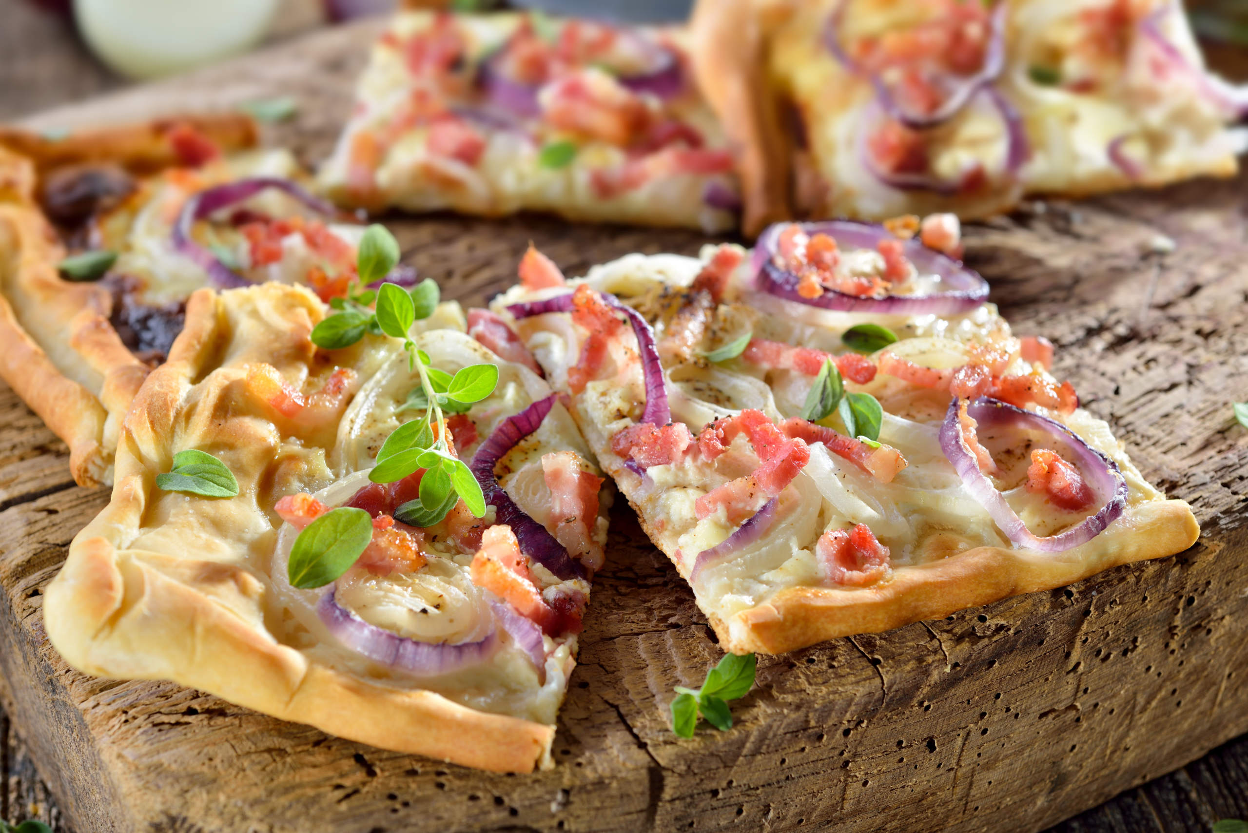 Elsässer Flammkuchen mit Zwiebeln und Speck rustikal auf altem Schneidbrett serviert – Traditional Alsatian tarte flambée with onions, bacon and sour cream served on a shabby cutting board