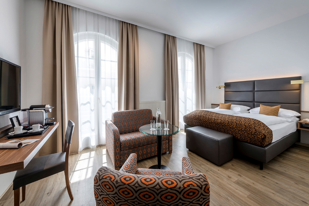 Deluxe Doppelzimmer des Hotel Nestroy Wien mit Doppelbett, zwei Sesseln und Schreibtisch